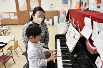先生と一緒にピアノに触れる子ども